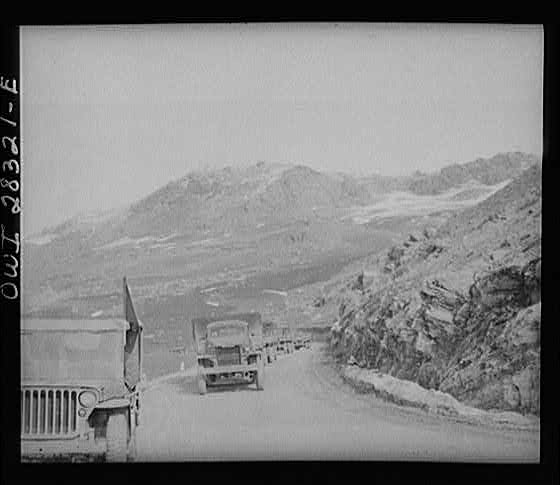 Somewhere in the Persian corridor. A United States Army truck convoy carrying supplies for the aid of Russia. Part of the convoy pulling up a mountain road. The convoy leader in a jeep at the left.